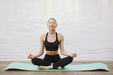 Su kenarında yoga yapan bir kadın.