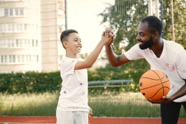 Siyahi baba ve çok ırklı oğlu basketbol sahasında birlikte oynuyorlar.