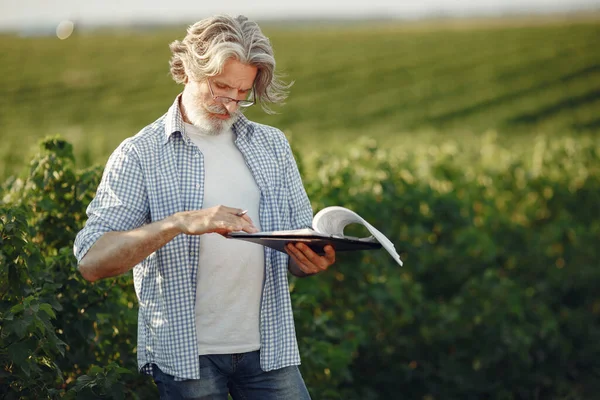 Antiguo granjero en camisa de pie en el campo con cuaderno —  Fotos de Stock
