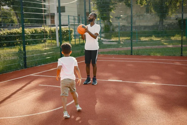 Homem negro com filho jogando basquete na quadra de basquete juntos — Fotografia de Stock