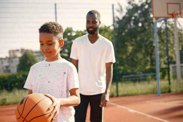 Pai negro com filho jogando basquete na quadra de basquete juntos — Fotografia de Stock