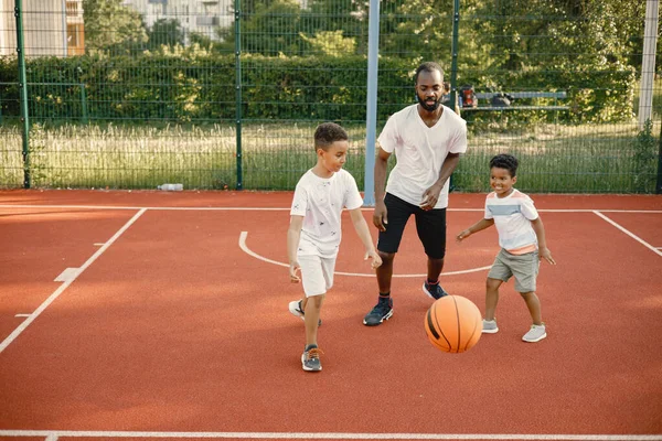 Preto pai com dois seus filhos multirraciais jogando basquete na quadra de basquete juntos — Fotografia de Stock
