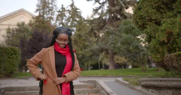 Чорна дівчина одягає навушники і піднімає телефон надворі — стокове відео