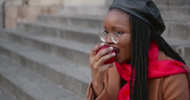 Genç siyah kız merdivenlerde elma yiyor.