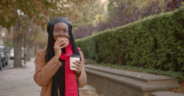 Jovencita negra con un croissant en las manos en medio de la calle — Vídeos de Stock