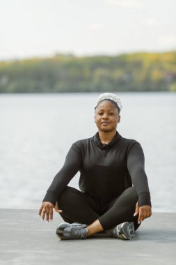 Afro-Amerikalı ve iri yarı kadın dışarıda yoga yapıyor.