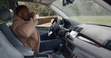 Genç adam arabada kahve içiyor.