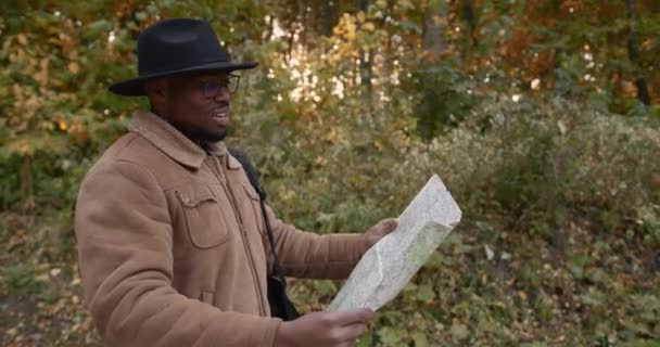 Young black traveler with a map walking in forest — Stock Video