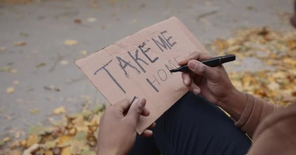 Młody czarny autostopowicz piszący na tekturze na drodze — Wideo stockowe