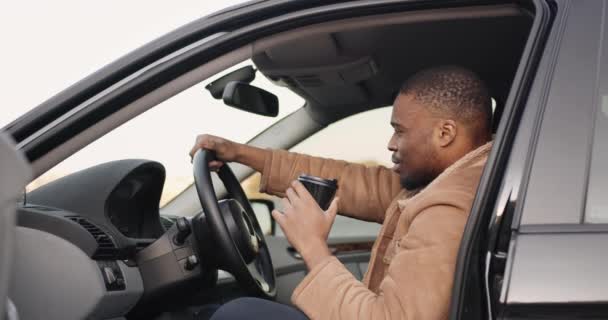 Direksiyonda siyah bir sürücü ve yanında kahve. — Stok video