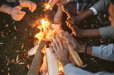 Genç arkadaşlar ormanda ateşin yanında ellerini ısıtıyorlar.
