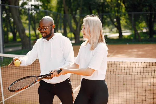 Uomo nero insegnare giovane donna a giocare a tennis — Foto Stock