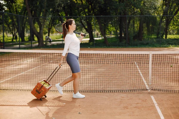 Donna con raquet e scatola di palle camminare sul campo — Foto Stock