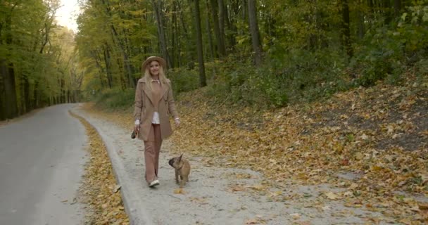 Glad ung kvinna promenader med hund längs vägen i höstparken — Stockvideo