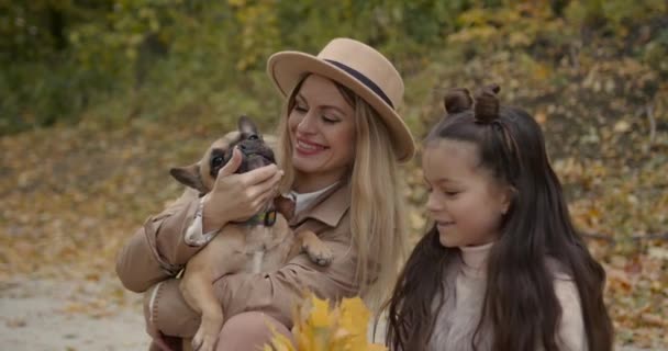 时尚的母亲和女儿坐在秋天的公园里和宠物玩耍 — 图库视频影像