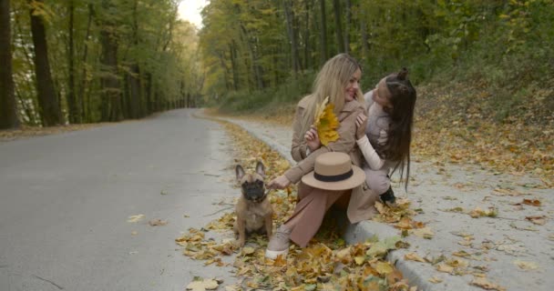 Snygg mamma och dotter leker med husdjur sitter i höstparken — Stockvideo