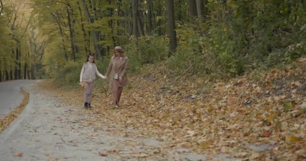 Νεαρή μητέρα με την κόρη της να τρέχει με κίτρινα φύλλα — Αρχείο Βίντεο