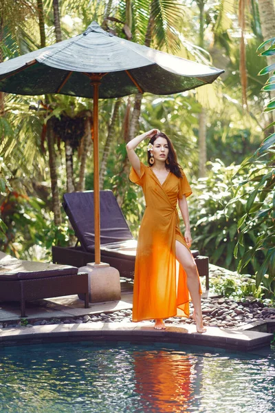 Kvinna i gul klänning står vid poolen på en Bali — Stockfoto