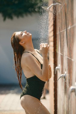 Beyaz kadın açık havada duşun altında mayo giymiş poz veriyor.