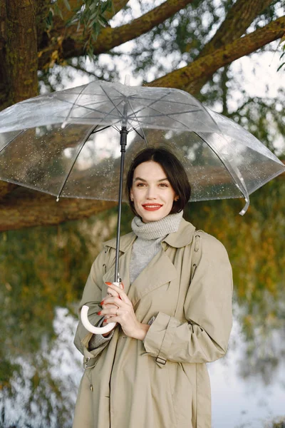 Portrait of a young woman in a coat under a transparent umbrella — Stock Photo, Image