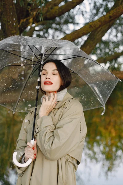 Porträt einer jungen Frau im Mantel unter einem durchsichtigen Regenschirm — Stockfoto