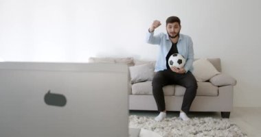 Genç bir Hint futbol fanatiği evde televizyon izliyor.