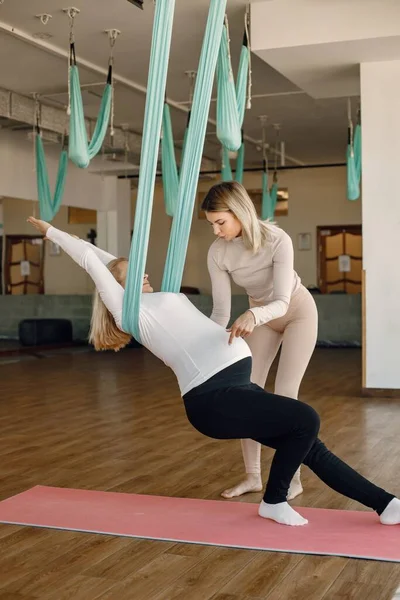 Тренер помогает беременной женщине делать упражнения с гамаком для йоги — стоковое фото