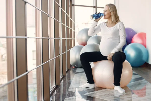 Pregnant woman drinking water in bright fitness studio — Fotografie, imagine de stoc