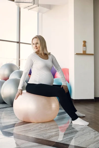 Pregnant woman doing fitness excercise in bright fitness studio — Fotografie, imagine de stoc