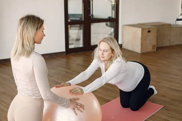 Entraîneur aidant la femme enceinte à faire des excercises avec un fitball — Photo