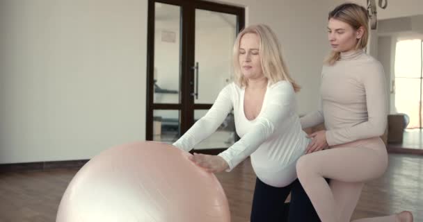 Šťastný trenér pomáhá těhotná žena, která dělá protahovací cvičení