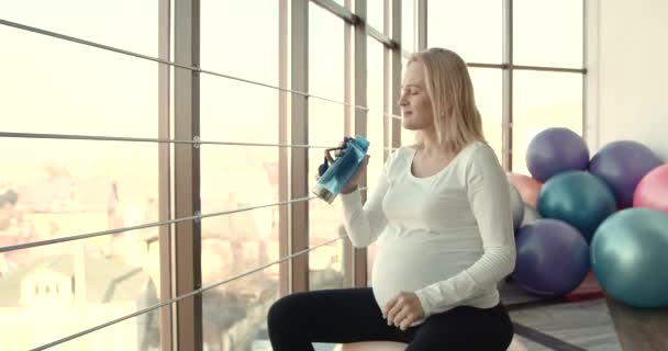 Вагітна жінка п'є воду в спортзалі — стокове відео