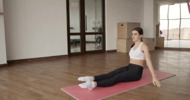 Spor salonundaki paspasın üzerinde gerinen atletik bir kadın.