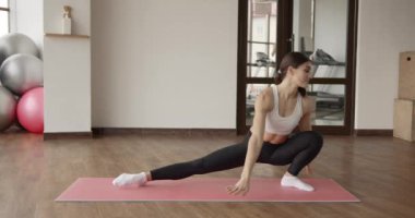 Spor salonundaki paspasın üzerinde gerinen atletik bir kadın.