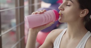 Yorgun kadın spor salonunda spor yaptıktan sonra su içer.