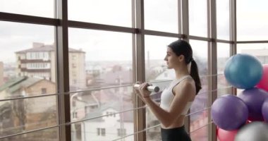Formda genç bir kadın spor salonunda dambıllarla egzersiz yapıyor.