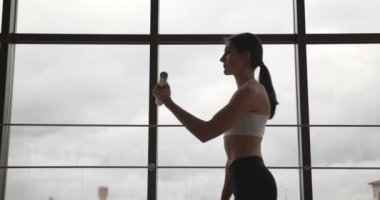 Formda genç bir kadın spor salonunda dambıllarla egzersiz yapıyor.