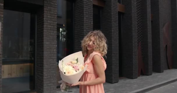 Glad elegant ung kvinna med blommor i staden — Stockvideo