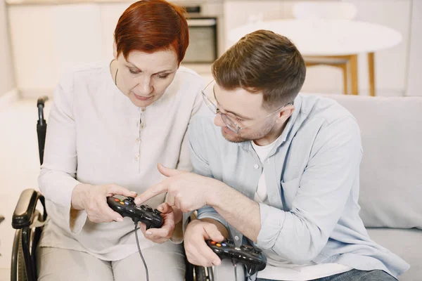 Kıdemli engelli kadın oğluyla video oyunu oynuyor.