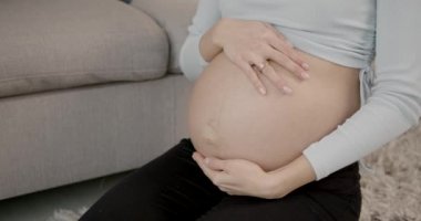 Genç ve güzel bir kadın oturma odasında otururken karnına dokunuyor.