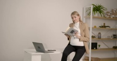 Genç ve şık hamile kadın ofiste oturmuş kitap okuyor.