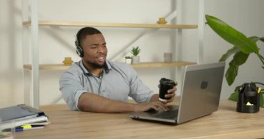 Laptop kullanan ve kahve içen kulaklıklı siyah bir adam.