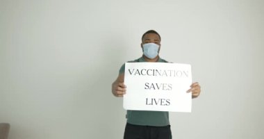 Anti-koronavirüs aşısını destekleyen posterleri olan siyah bir genç adam.