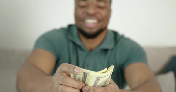 Joven negro cuenta el dinero sentado en el sofá — Vídeo de stock