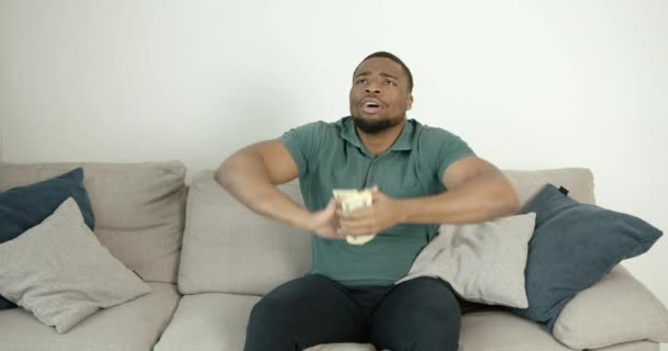 Czarny młody człowiek liczy pieniądze siedząc na kanapie — Wideo stockowe