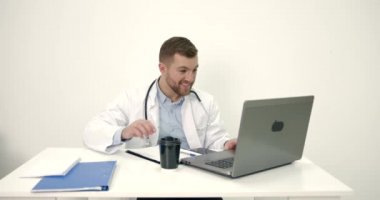 Erkek doktor ofiste dizüstü bilgisayarla çalışıyor.