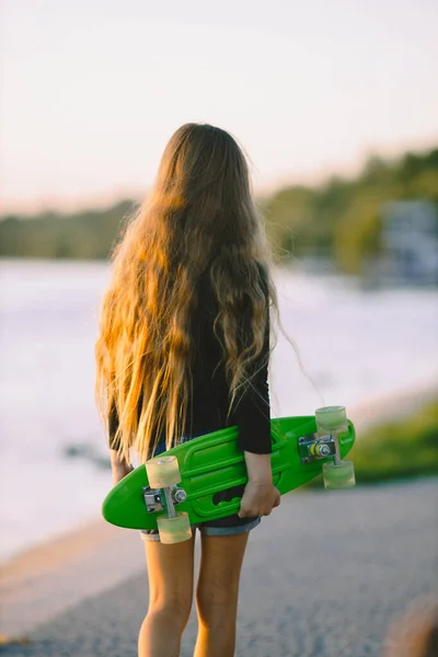 Teenage girl with skateboard sitting by lake — 스톡 사진