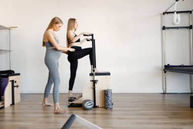 Hamile bir kadın ve hamile bir koç spor salonunda esneme hareketleri yapıyor.