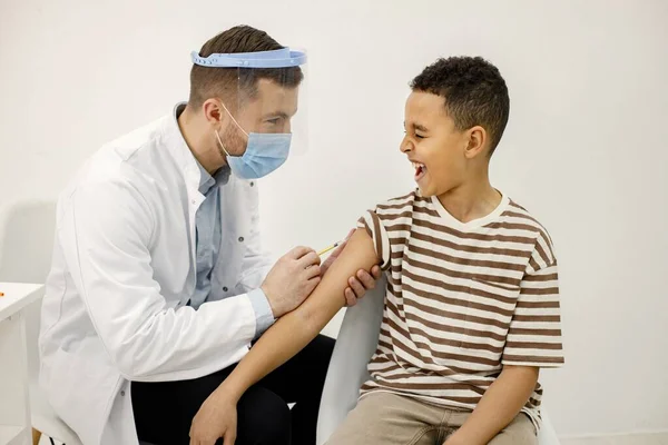 Male doctor doing a vaccination to a multiracional boy — Zdjęcie stockowe