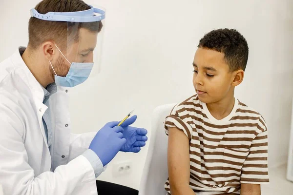 Male doctor doing a vaccination to a multiracional boy — Zdjęcie stockowe